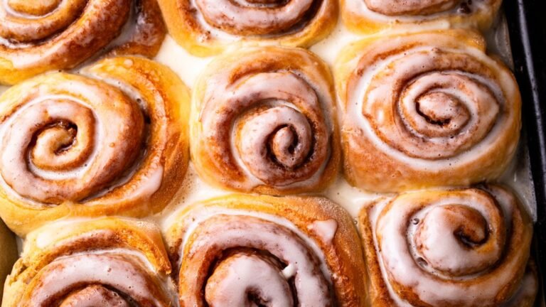 Cinnamon rolls with white icing cooling in a baking tray, close-up of swirled pastries.