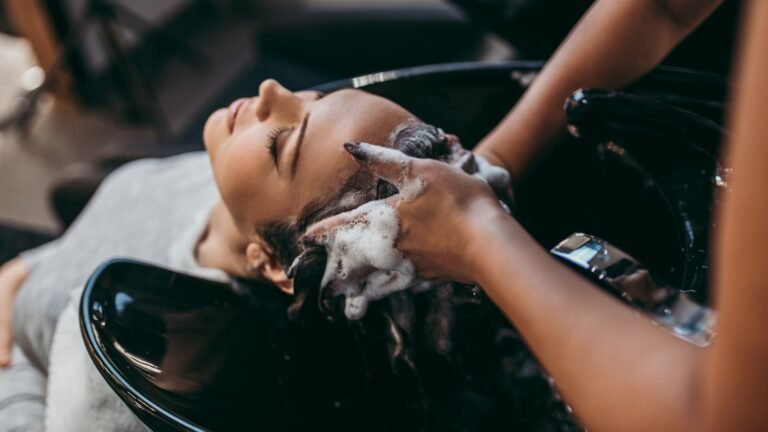 Woman reclining with head back as a stylist washes her hair over a black salon sink, shampoo lathering.