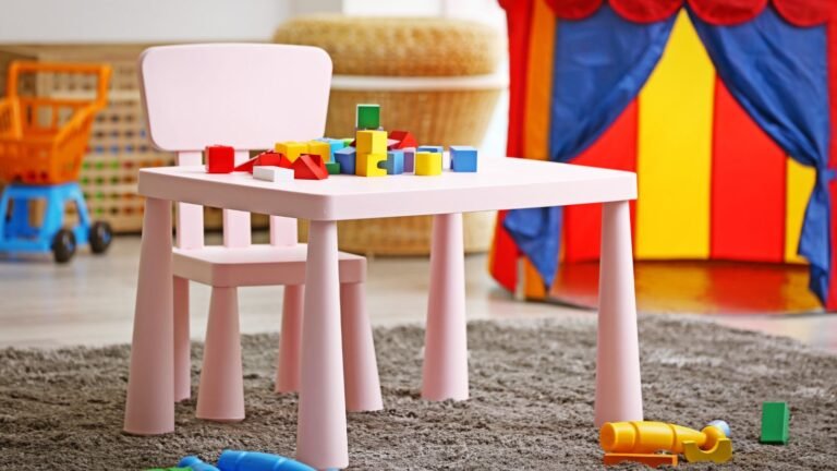 Pink child’s table with scattered colorful wooden blocks and toys on a gray carpeted floor in a playroom with a colorful tent in the background