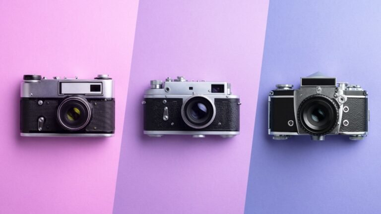 Three vintage film cameras lined up on pastel pink, lavender, and blue backgrounds.