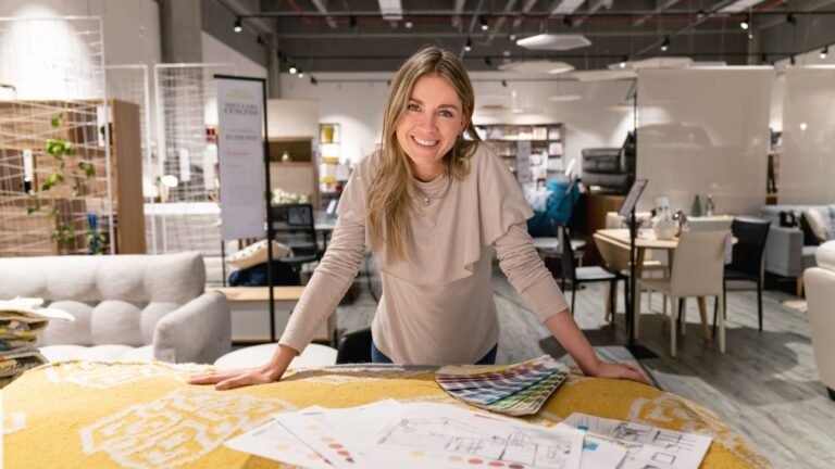 Smiling woman leans over a yellow fabric table with color swatches in a furniture showroom.
