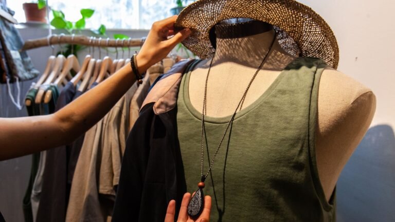 Mannequin wearing a green tank top, layered necklace, as a shopper adjusts a straw hat on its head in a clothing store